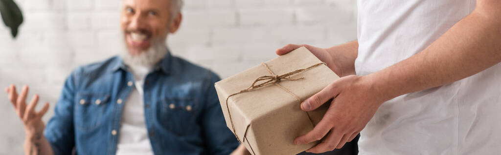 Мужчина держит подарочную коробку рядом с размытым отцом дома, баннер  - Фото, изображение