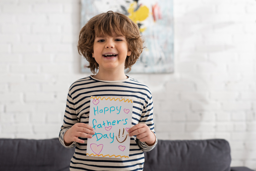 Lächelnder Junge mit Geschenkkarte mit Glückwunsch-Vatertag-Schriftzug  - Foto, Bild