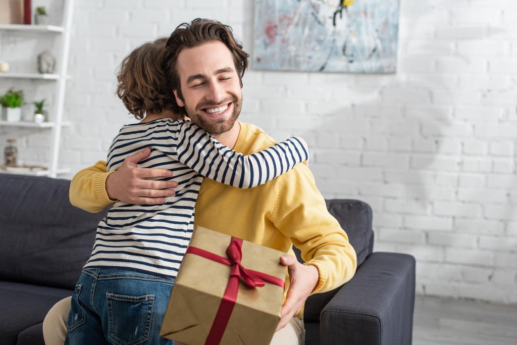 Gülümseyen adam oğluna sarılıyor ve evde hediyesini tutuyor.  - Fotoğraf, Görsel