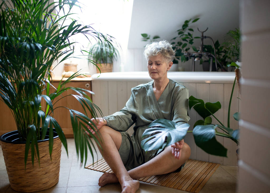 Ηλικιωμένη γυναίκα που κάνει γιόγκα στο μπάνιο στο σπίτι, χαλαρώστε και αυτο-φροντίδα έννοια. - Φωτογραφία, εικόνα