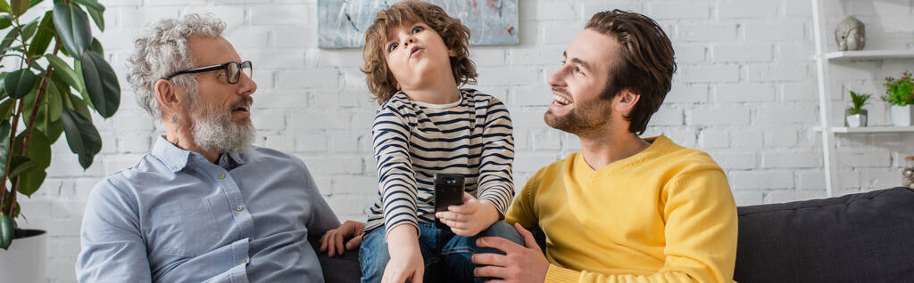 Χαμογελώντας πατέρας και παππούς κοιτάζοντας το παιδί με τηλεχειριστήριο, πανό  - Φωτογραφία, εικόνα