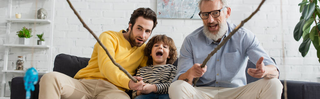 Men and excited child playing toy fishing in living room, banner  - Photo, Image