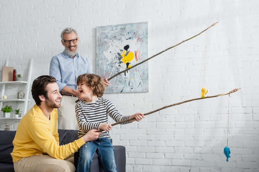 Ojciec i wesoły syn bawią się w łowienie zabawek w pobliżu rozmytego dziadka  - Zdjęcie, obraz
