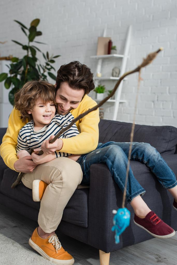 Счастливый отец и ребенок играют в игрушечную рыбалку на диване  - Фото, изображение
