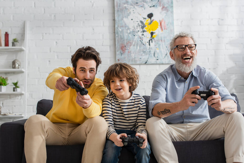 KYIV, UCRAINA - 12 APRILE 2021: Ragazzo sorridente che gioca al videogioco con padre e nonno  - Foto, immagini