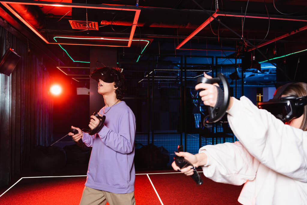 verbaasd jongen in vr headset gaming in de buurt van een vriend in de speelzone - Foto, afbeelding