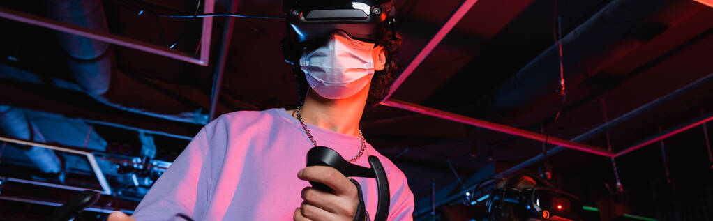 парень-подросток в медицинской маске и видеогарнитуре игры в игровой зоне, баннер - Фото, изображение