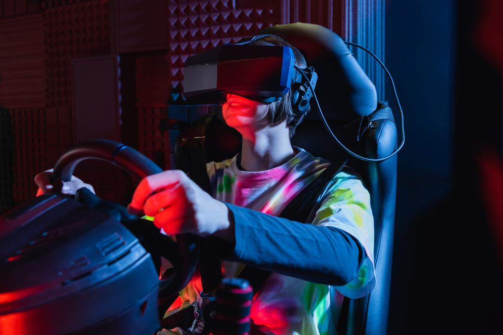 gelukkig tiener jongen houden stuurwiel terwijl gaming op auto simulator - Foto, afbeelding