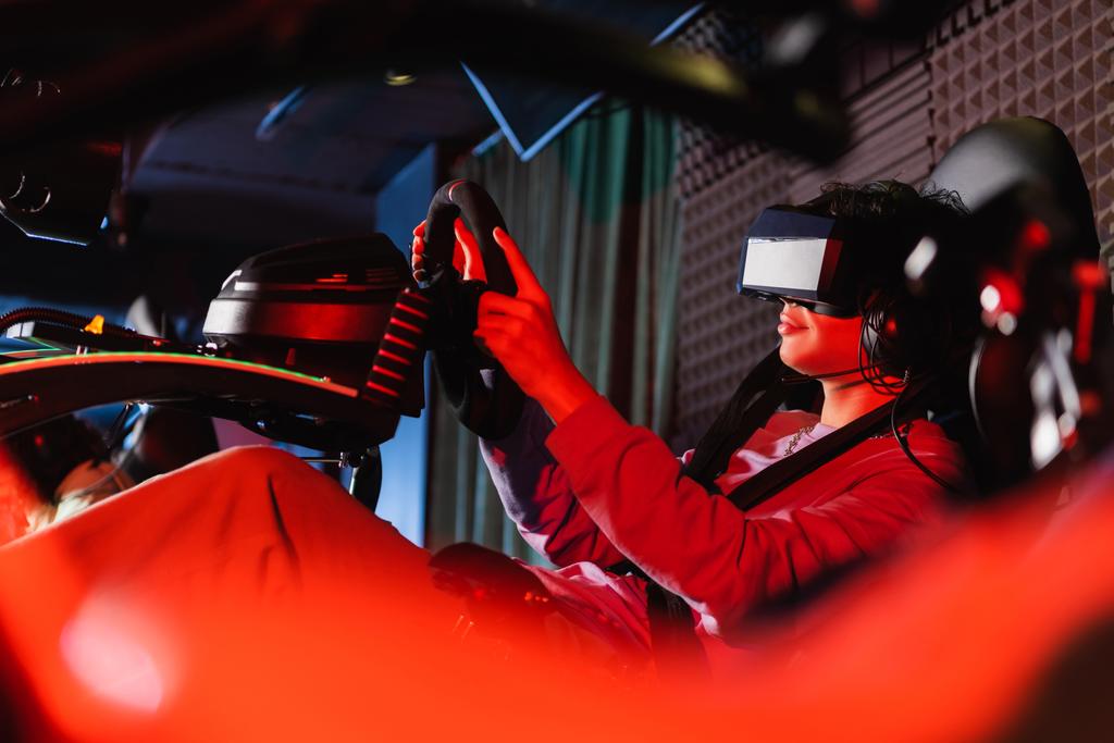 tiener in vr headset gaming op auto race simulator op wazig voorgrond - Foto, afbeelding