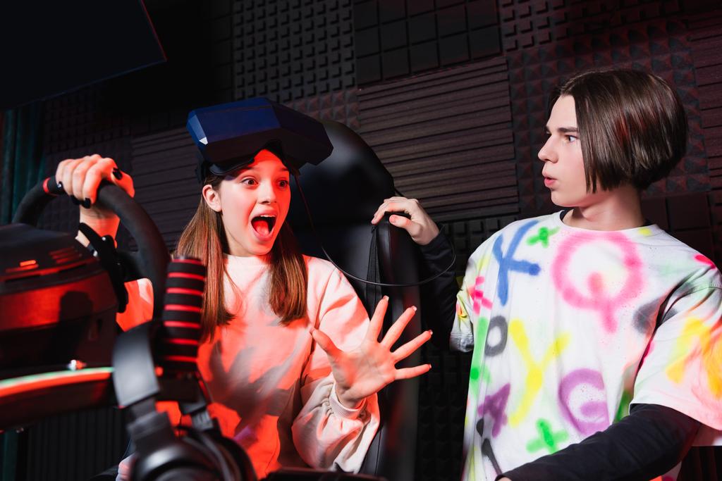 užaslá dívka na auto simulátor gestikulace poblíž překvapený přítel - Fotografie, Obrázek