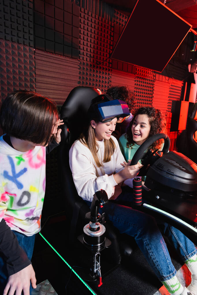 adolescentes inter-raciais alegres rindo perto menina espantada no simulador de carro - Foto, Imagem