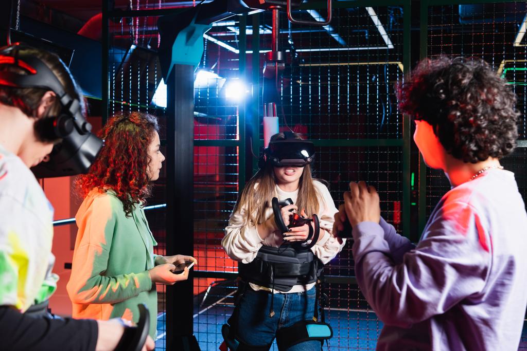 Heyecanlı genç kız, çok ırklı arkadaşlarının yanında, VR kulaklıkla oynuyor. - Fotoğraf, Görsel