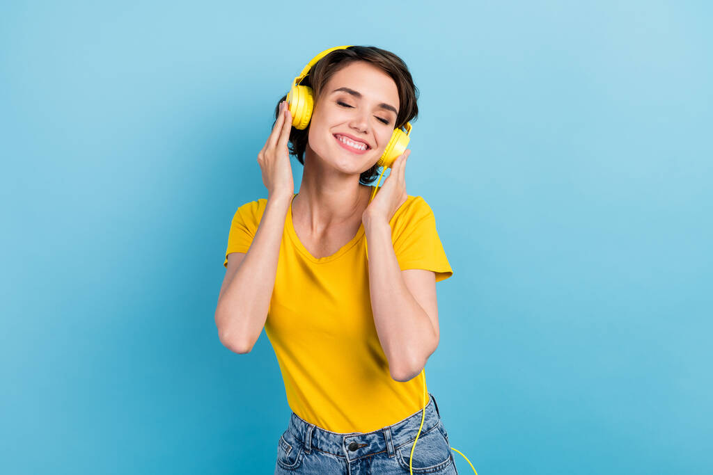 Фото очаровательной молодой девушки с закрытыми глазами слушать музыку носить наушники желтые футболки изолированы синий цвет фона - Фото, изображение