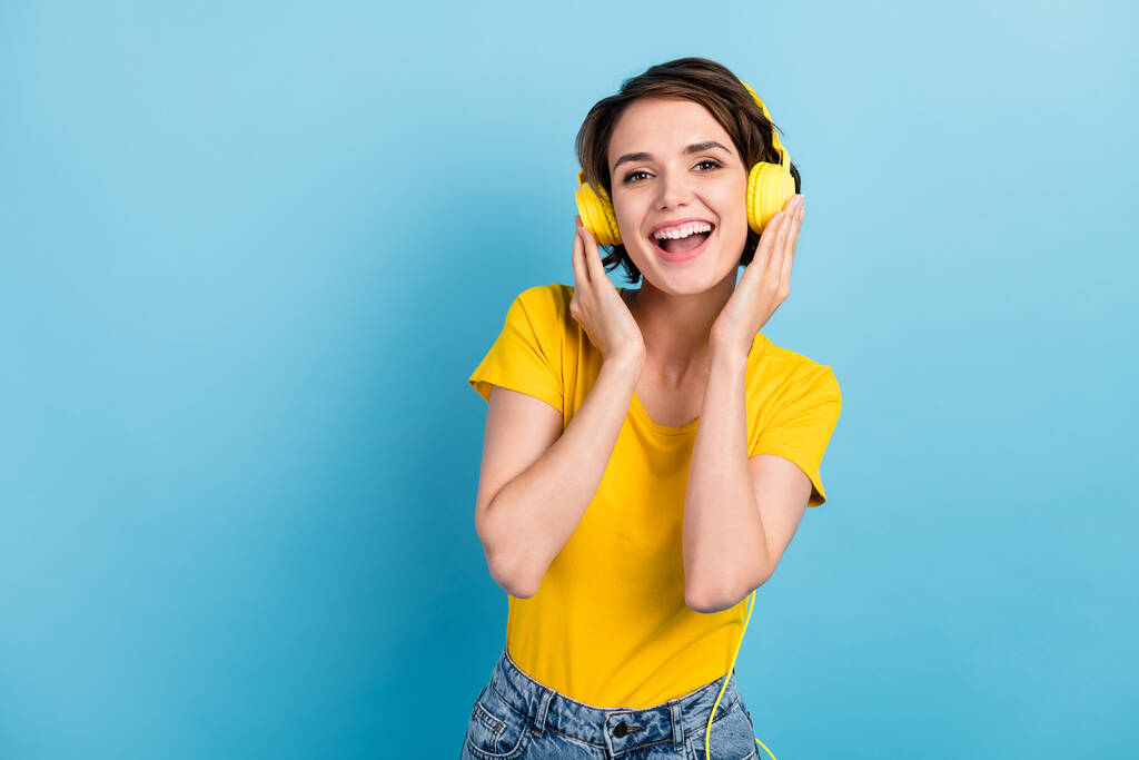 Foto de chica joven encantadora escuchar música boca abierta mirar cámara usar auriculares camiseta amarilla aislado color azul fondo - Foto, Imagen