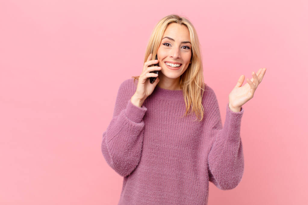 young blonde woman feeling happy, surprised realizing a solution or idea and talking with a smartphone - Photo, Image