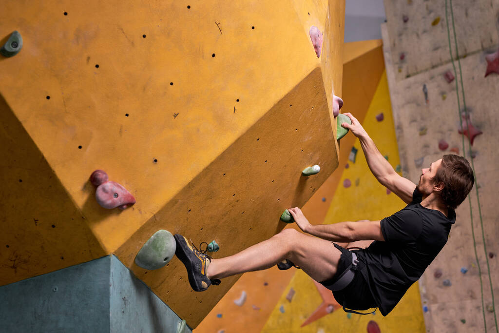 Mladý muž vyleze na umělou skalní stěnu, sport a fitness koncepce, boční pohled - Fotografie, Obrázek