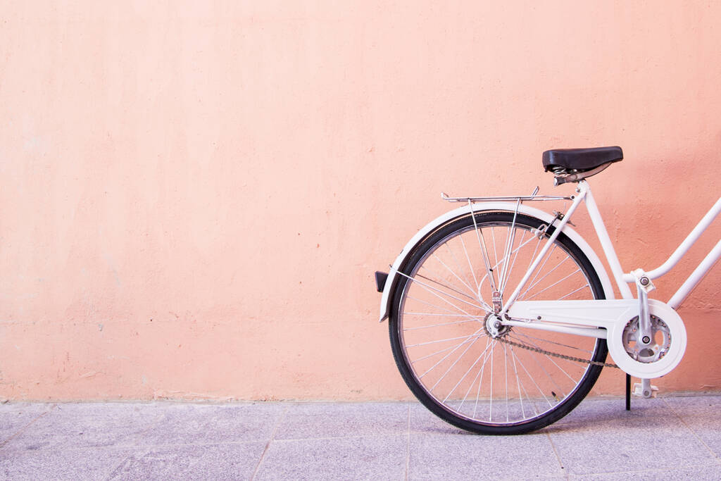 Eine Nahaufnahme eines weißen Fahrrads, das in der Nähe einer Pfirsichwand geparkt ist - perfekt für ästhetische Tapeten - Foto, Bild