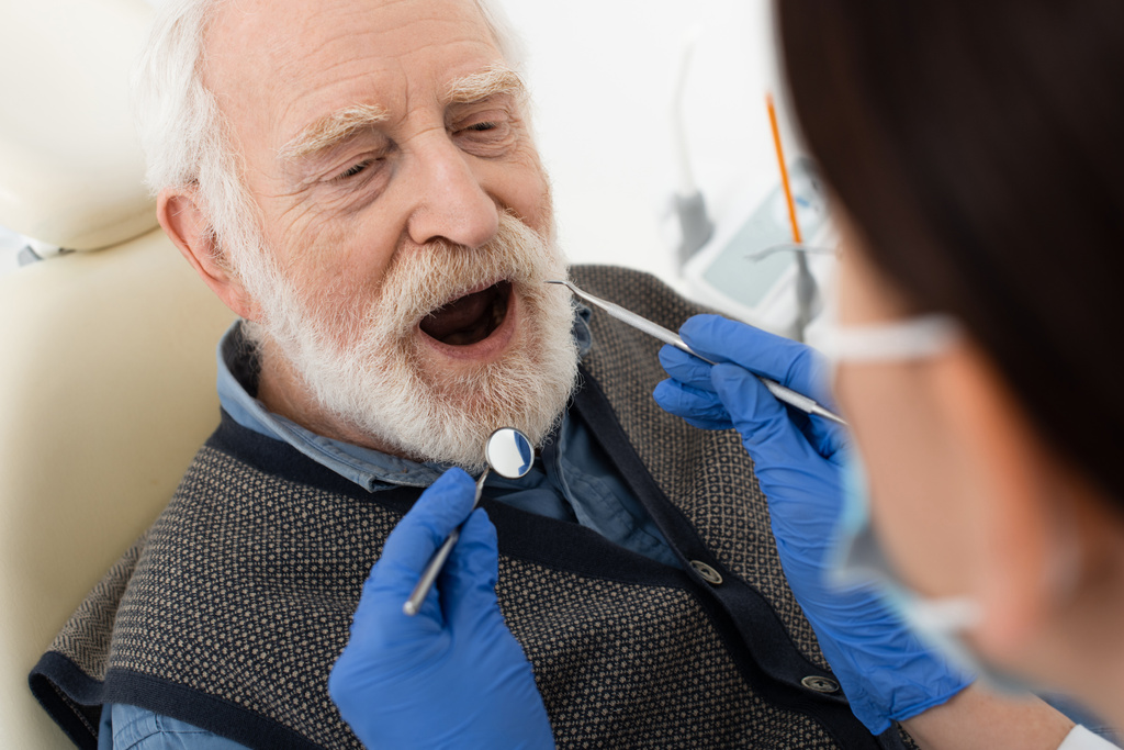 старший чоловік має обстеження зубів стоматологом в латексних рукавичках з зондом і дзеркалом в клініці
 - Фото, зображення