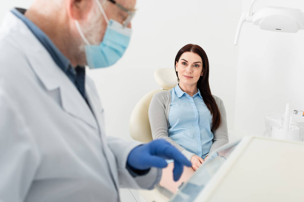positive woman sitting in dental chair and looking at dentist standing near equipment in clinic - Photo, Image