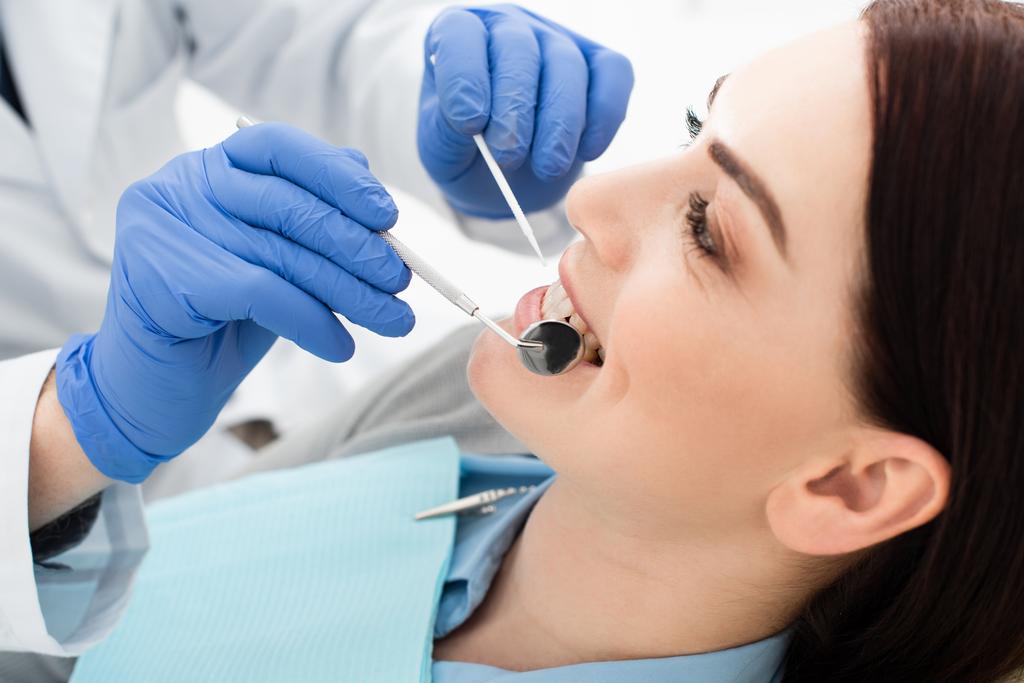 vista de cerca de la mujer adulta que tiene examen de dientes por el médico en guantes de látex en la clínica - Foto, Imagen