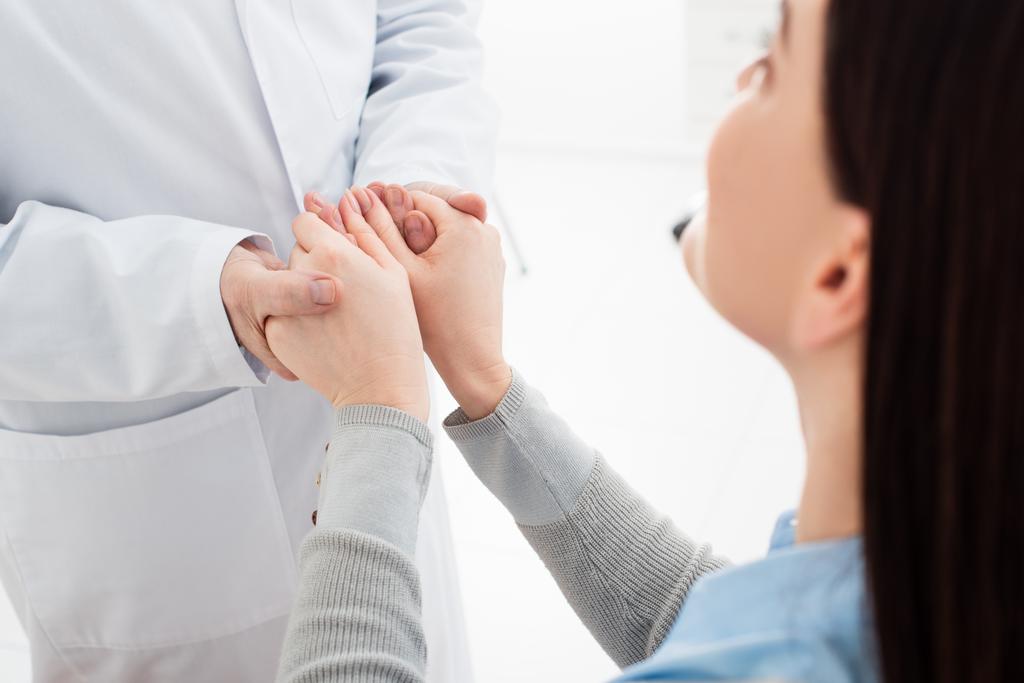 brünette Frau sitzt und hält Hände des Arztes in Klinik - Foto, Bild