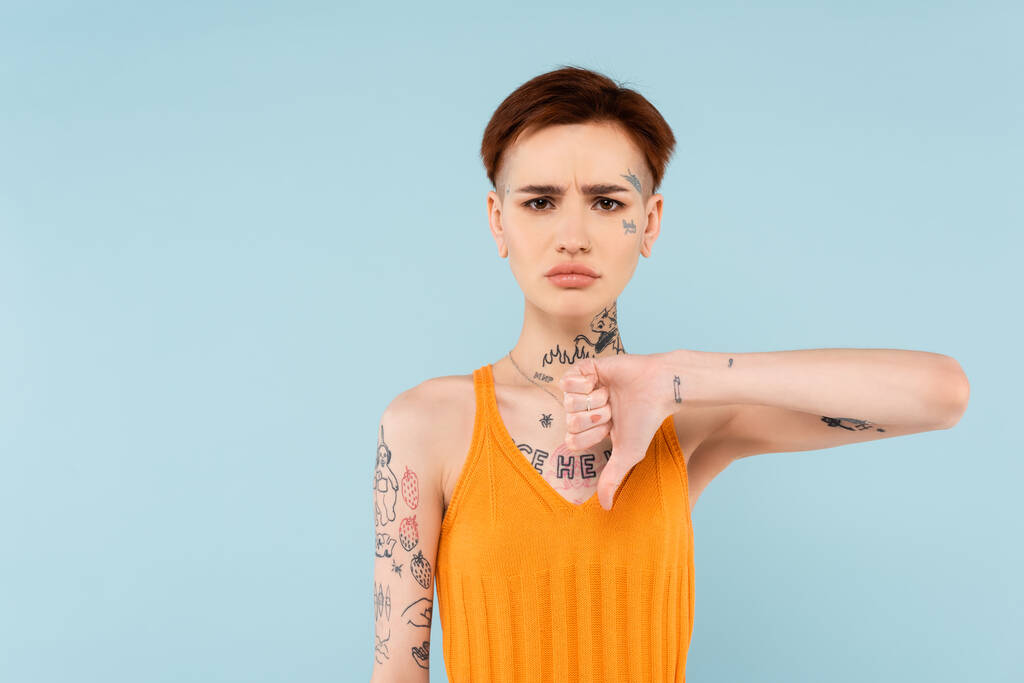δυσαρεστημένη και γυναίκα με τατουάζ που δείχνει τον αντίχειρα κάτω απομονωμένο στο μπλε  - Φωτογραφία, εικόνα