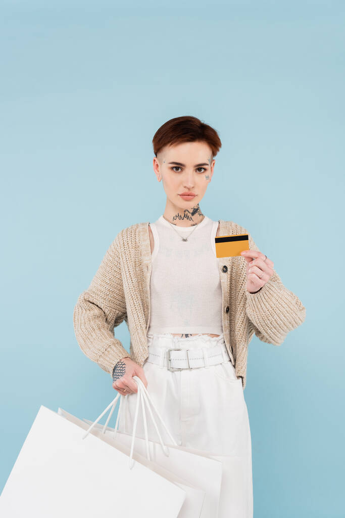 fiatal tetovált nő gazdaság hitelkártya és bevásárló táskák elszigetelt kék - Fotó, kép