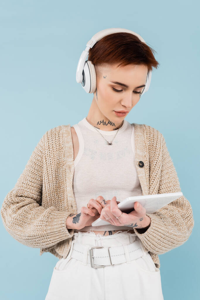 Nuori nainen tatuoinnit digitaalinen tabletti ja kuunnella musiikkia langattomat kuulokkeet eristetty sininen - Valokuva, kuva
