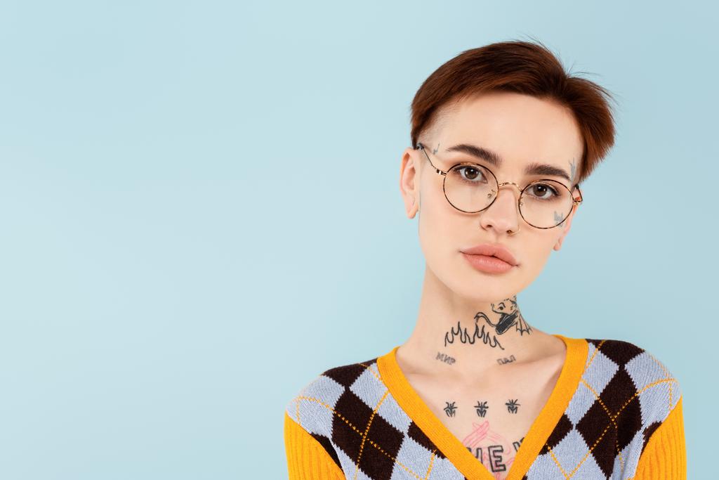 nuori tatuoitu nainen silmälaseissa katselee kameraa eristettynä siniseen - Valokuva, kuva