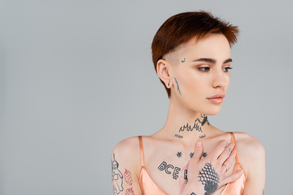 mladá tetovaná žena dívá pryč izolované na šedé  - Fotografie, Obrázek