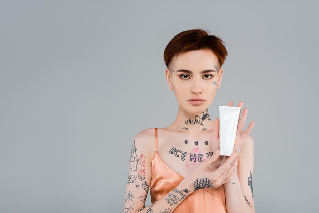 giovane donna tatuata tubo di tenuta con prodotto cosmetico isolato su grigio - Foto, immagini