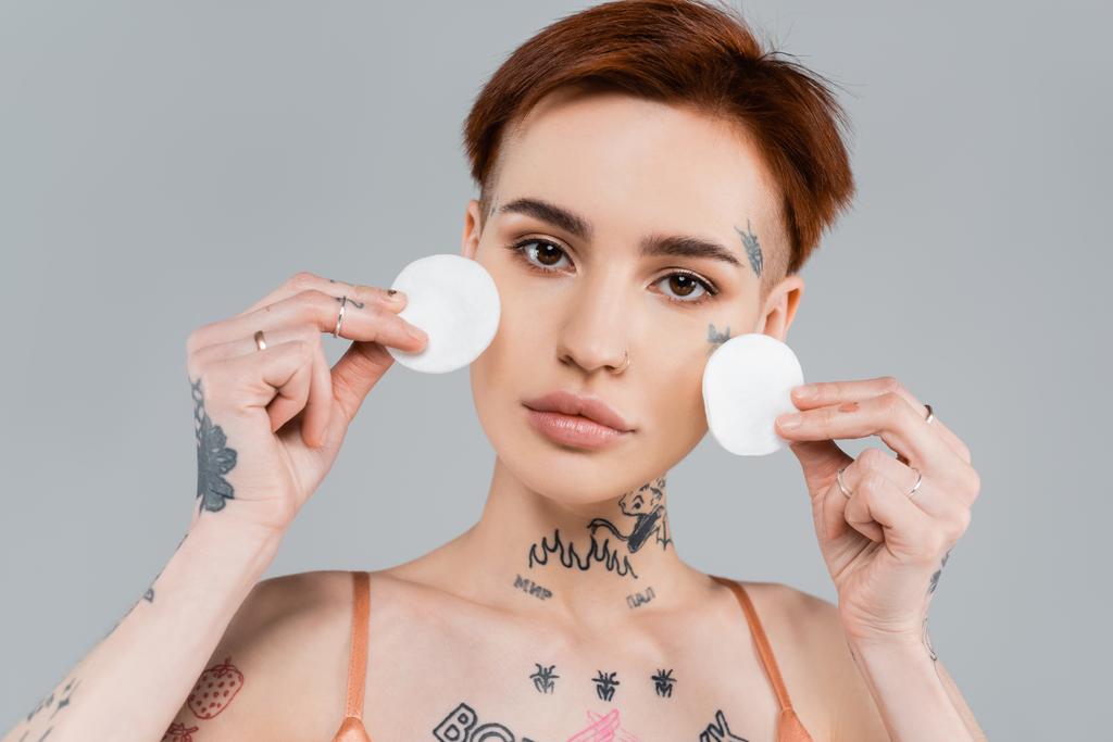 young tattooed woman holding cotton pads isolated on grey  - Photo, Image
