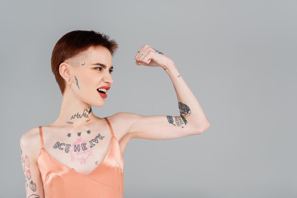 tatuato giovane donna con labbra rosse mostrando muscolo isolato su grigio  - Foto, immagini