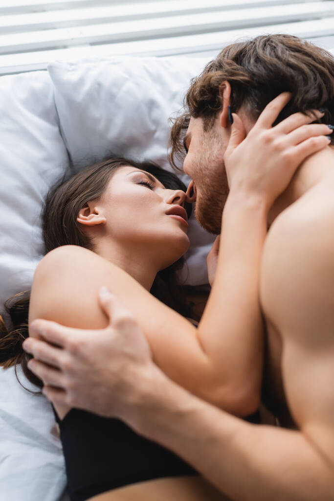 Hemdloser Mann küsst hübsche Frau auf Bett  - Foto, Bild