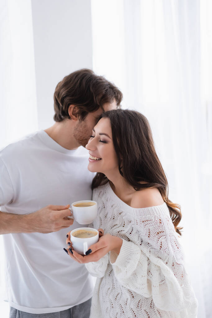 Homem beijando namorada alegre em camisola de malha com café  - Foto, Imagem