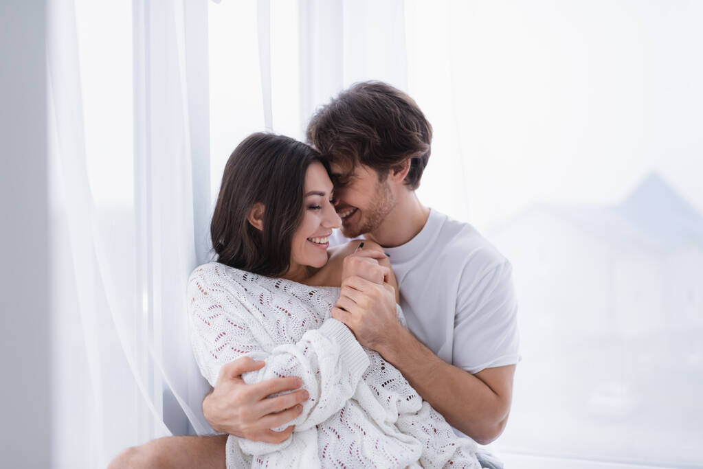 Lächelnder Mann umarmt Freundin nahe Vorhang zu Hause  - Foto, Bild