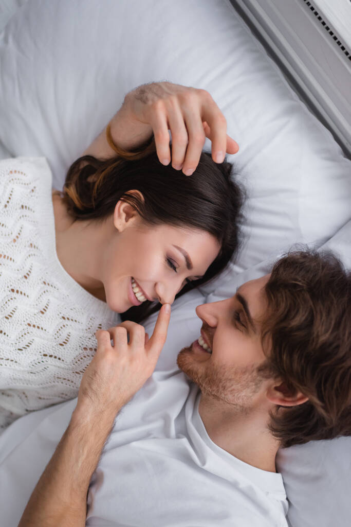 Pohled shora na muže dotýkajícího se nosu usměvavé přítelkyně na posteli  - Fotografie, Obrázek