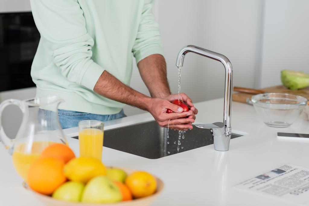 częściowy widok człowieka mycie pomidorów wiśniowych w pobliżu owoców i soku pomarańczowego w kuchni - Zdjęcie, obraz