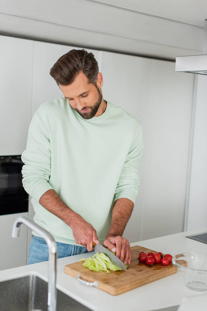 hombre cortar lechuga fresca cerca de tomates cherry mientras prepara el desayuno - Foto, Imagen
