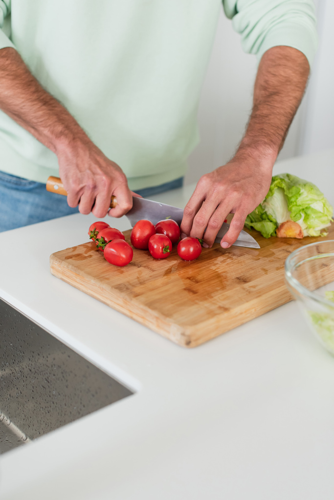 частковий вид людини, що ріже стиглі вишневі помідори на кухні
 - Фото, зображення