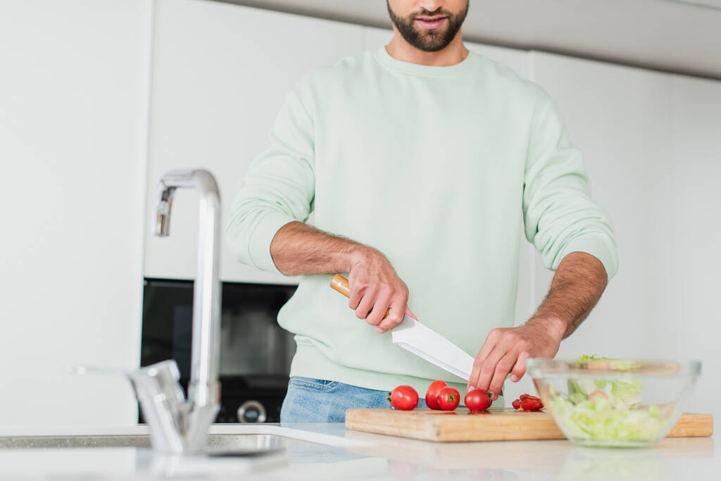 前景のぼやけたキッチンで野菜サラダを作る男の部分的な見方 - 写真・画像