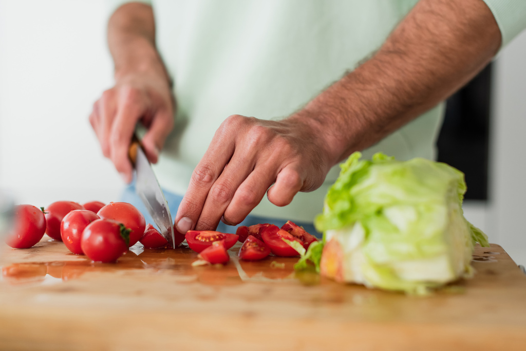 обрезанный вид человека, режущего помидоры черри возле свежего салата на кухне - Фото, изображение