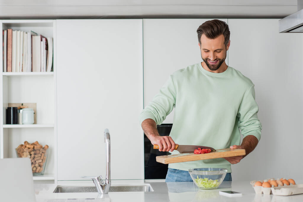 pozitivní muž usmívá při vaření snídaně v kuchyni - Fotografie, Obrázek