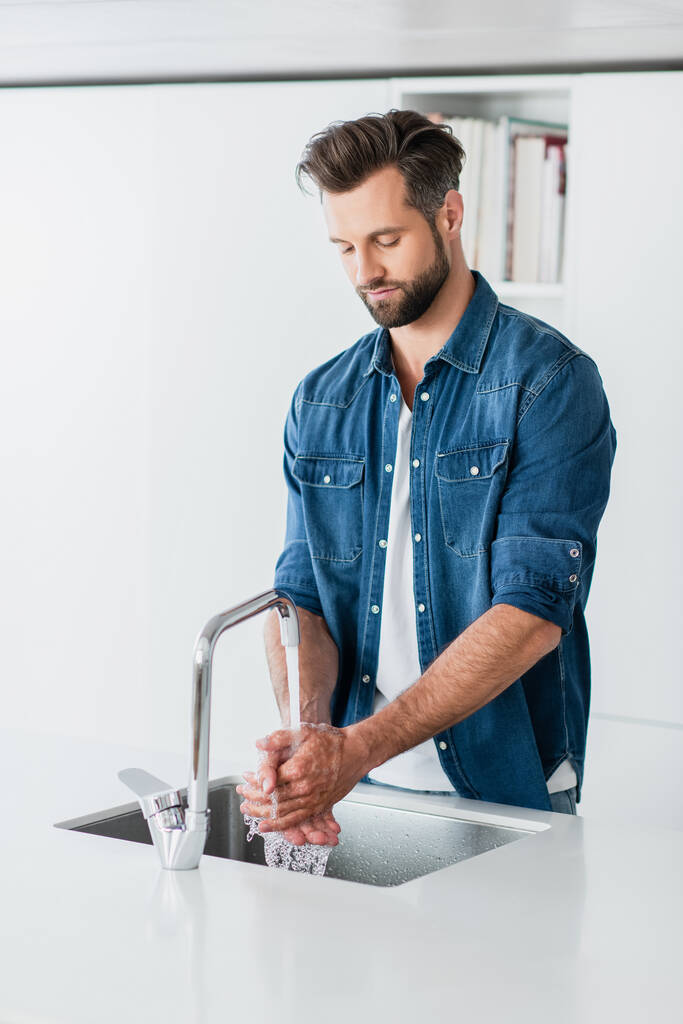 дорослий чоловік в джинсовій сорочці миє руки вдома
 - Фото, зображення