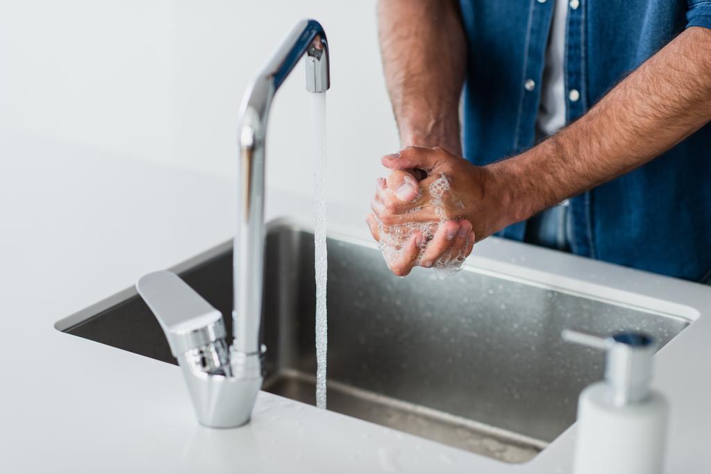 vista parcial del hombre lavándose las manos en casa en primer plano borroso - Foto, imagen