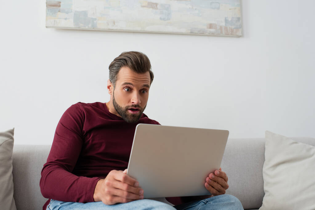 surprised man sitting on sofa and looking at laptop - Photo, Image
