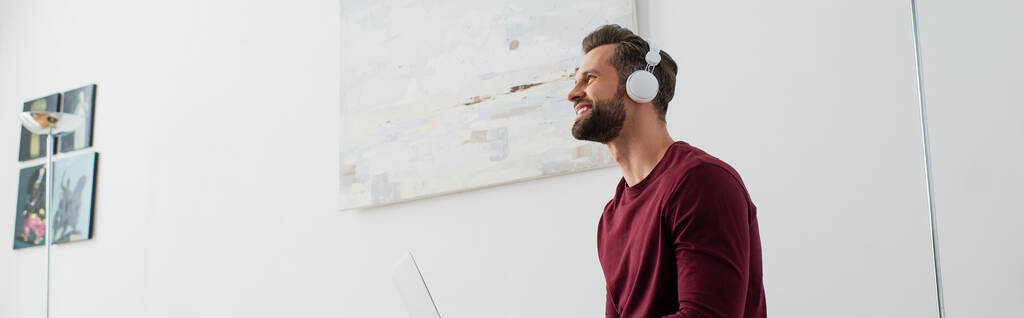 sonriente hombre mirando hacia otro lado mientras escucha música en auriculares inalámbricos, banner - Foto, Imagen