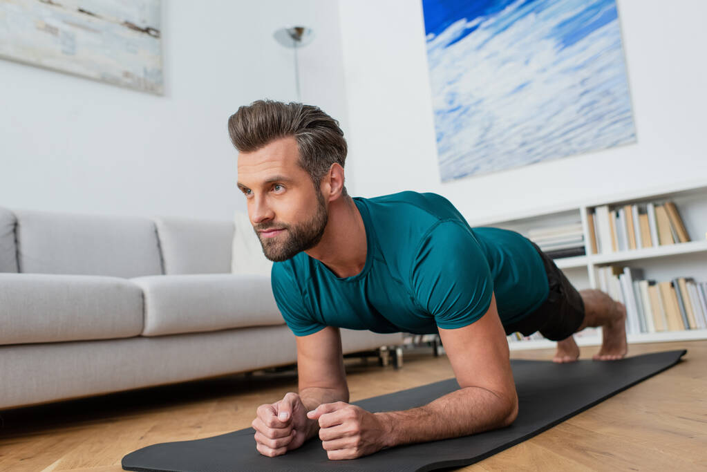 blootsvoets man het beoefenen van yoga in plank poseren thuis - Foto, afbeelding