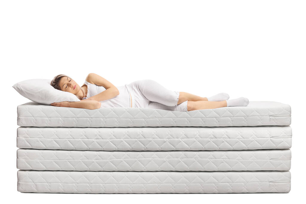 Jovem de pijama dormindo em pilha de colchões isolados sobre fundo branco - Foto, Imagem