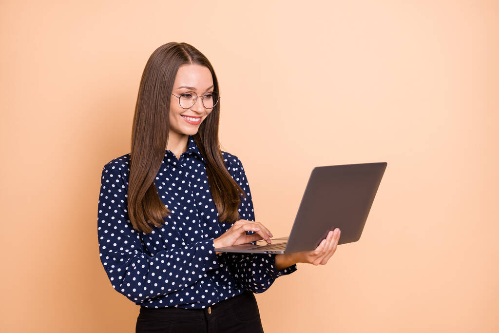фото молодой деловой женщины счастливой позитивной улыбкой смотреть просматривать ноутбук программист изолирован на бежевом фоне - Фото, изображение